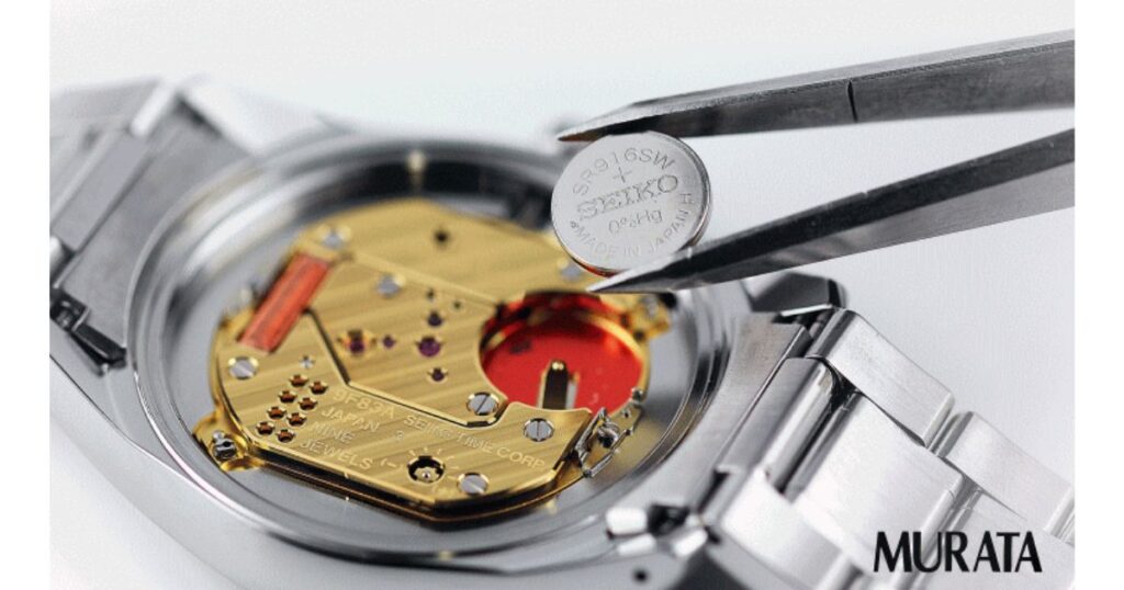 ピンセットで小さなボタン電池をつまみ、腕時計の内部にセットしようとしている様子