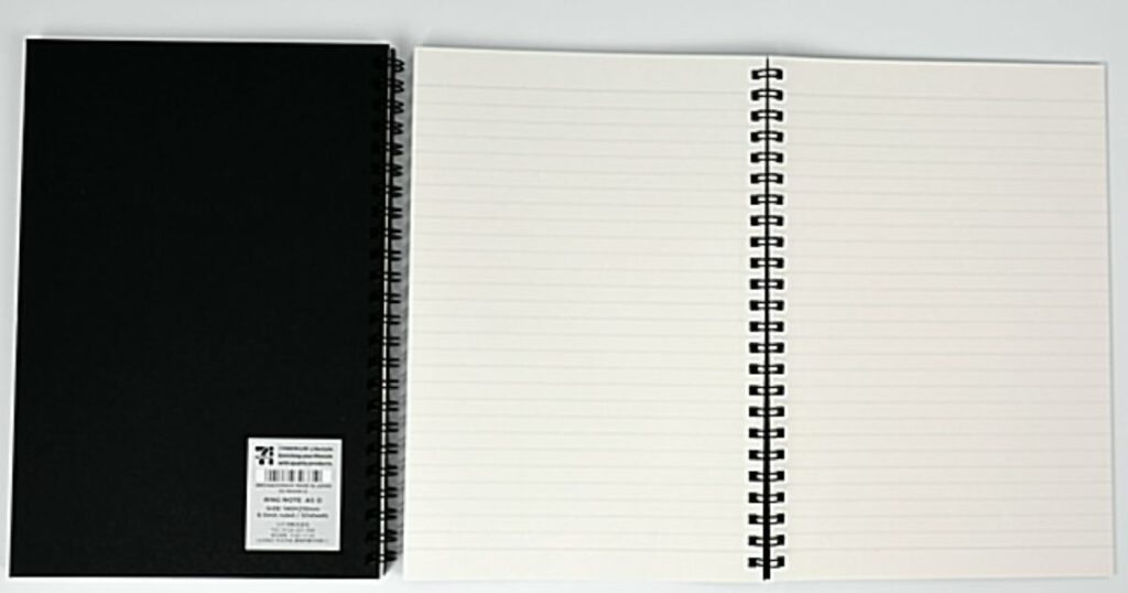 開かれた状態のリングノートの実物写真。左側は裏返された黒い表紙でラベルが貼られており、右側はクリーム色の横罫線入りのページ。