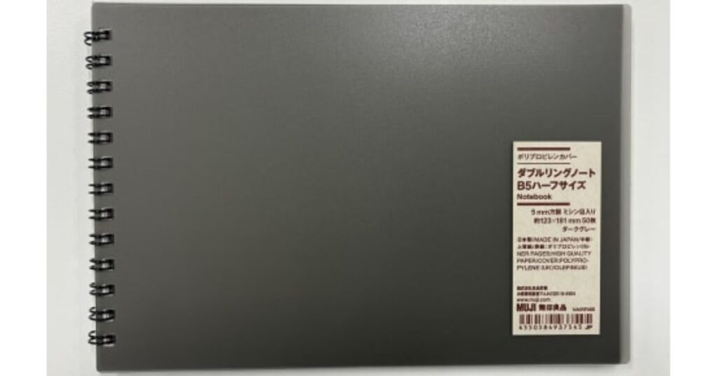 グレーの無地の表紙で左側にダブルリングがあり、右下に製品ラベルが貼られた無印良品のノート。