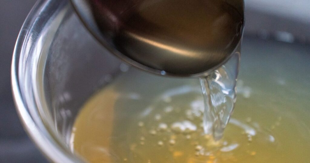 お玉からボウルに注がれている、透き通った黄金色のおでんのつゆ(出汁)