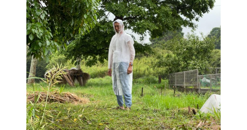 屋外でオーソドックスな半透明のビニール製レインコート(カッパ)を着用して立っている男性