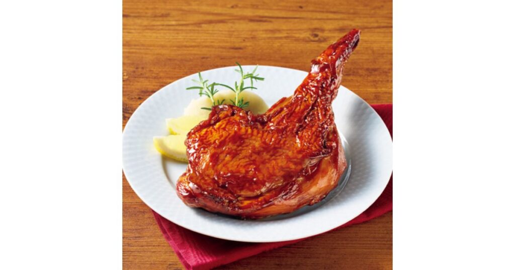 白いお皿に盛り付けられた、照りのある骨付きローストチキンの画像