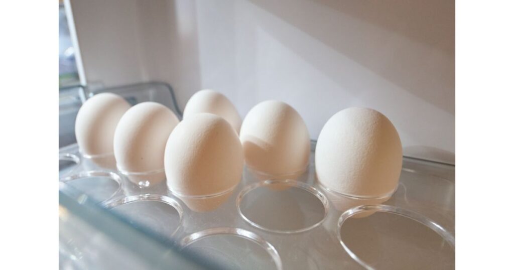 冷蔵庫のドアポケットにある透明な卵ケースに、綺麗に並べられて保存されている白い卵の写真
