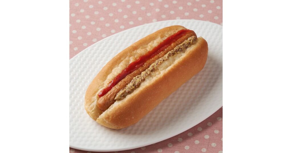 ピンクの水玉背景の白いお皿に乗せられた、ボリュームのあるホットドッグ（ファミリーマートの商品イメージ）