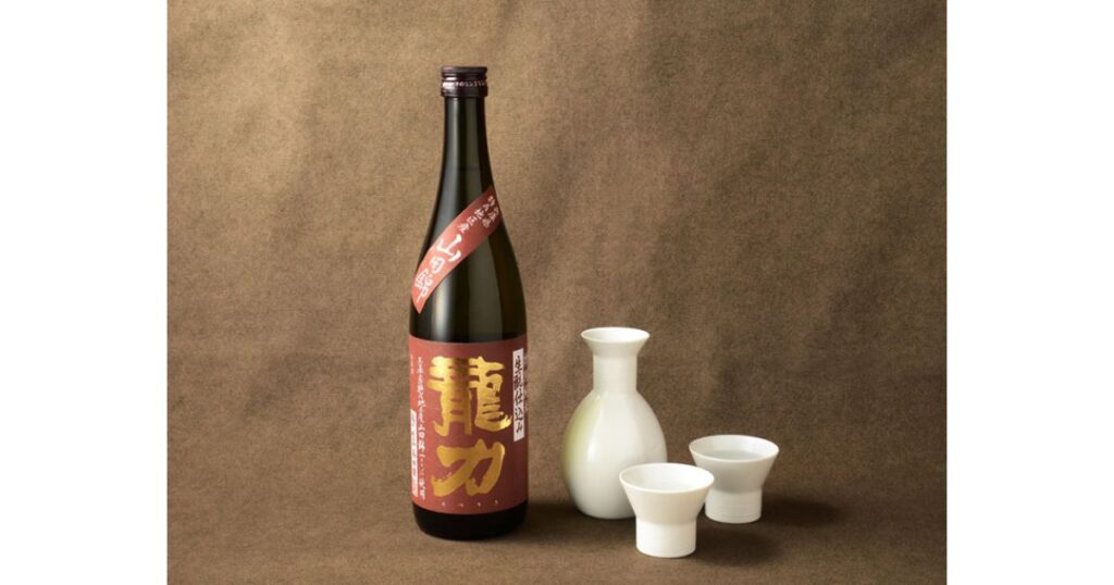 赤いラベルの日本酒「龍力」のボトルと白い徳利、2つのお猪口