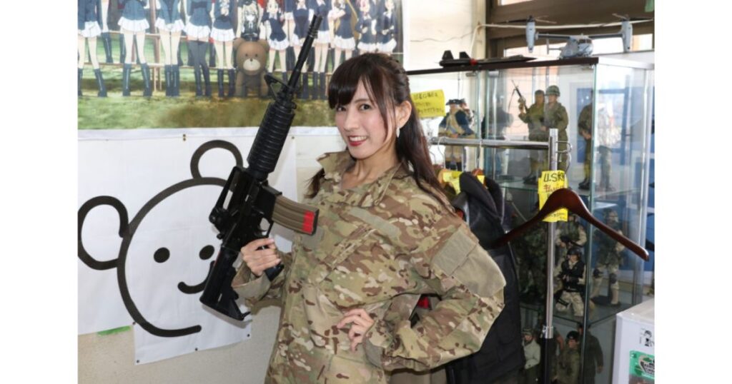 ミリタリーグッズが多数展示された店内で、迷彩服を着てアサルトライフルを構える女性