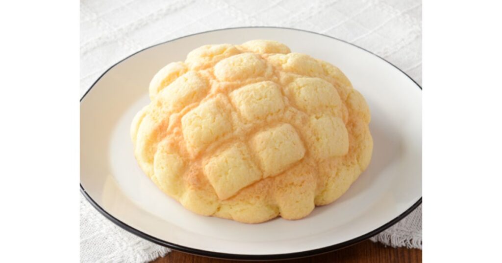 黒い縁取りの白いお皿の上に乗った、綺麗な網目模様がある定番のふんわりとしたメロンパン