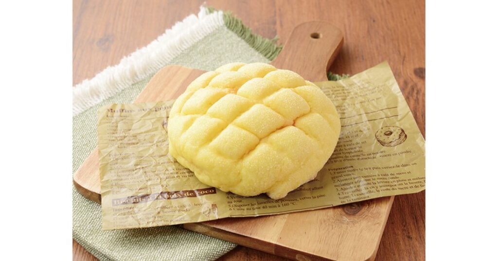 木製ボードに敷かれた英字柄のクッキングペーパーの上に乗った、表面に砂糖がキラキラと光るメロンパン