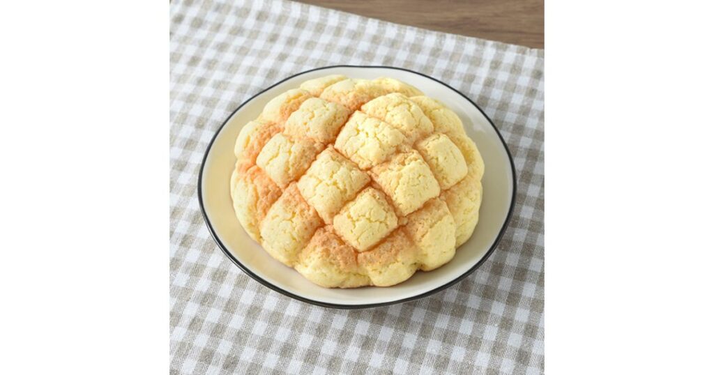 チェック柄のランチョンマットに置かれた白いお皿と、その上の美味しそうなコンビニメロンパン