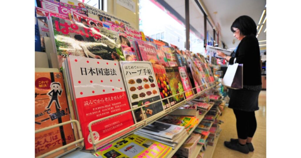 コンビニの窓際にある雑誌コーナーで、書籍や雑誌が並ぶ棚の前に立ち読みをしている女性の写真