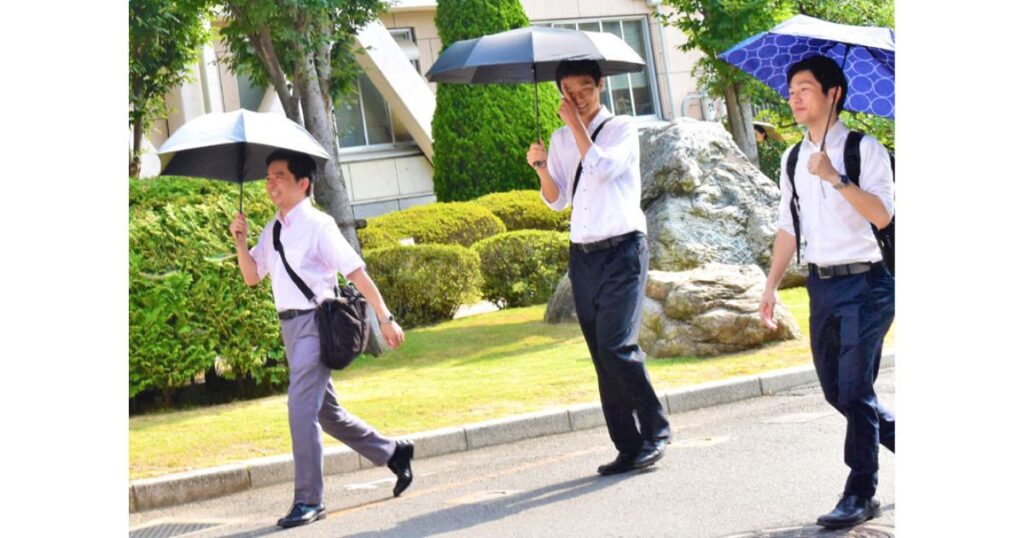夏の強い日差しの中、熱中症対策として日傘をさして通勤するスーツ姿の男性たち（日傘男子）
