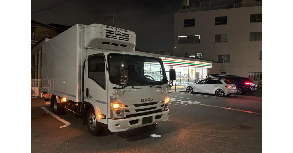 夜間のセブン-イレブン駐車場に停まっている白い中型・大型トラック。大型車が駐車可能な広さのイメージ