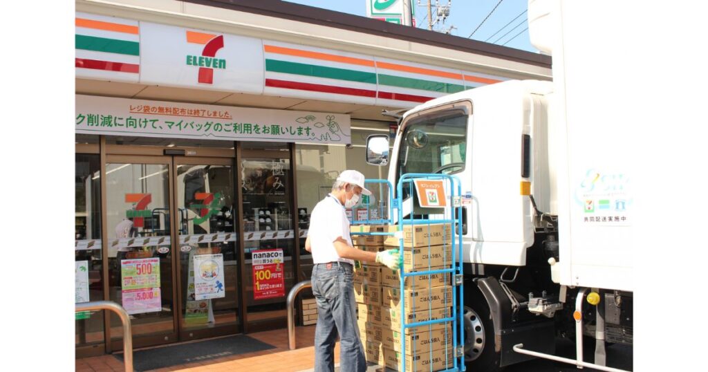 セブンイレブンの店舗前で、配送トラックから商品を台車に積み下ろしている納品作業員