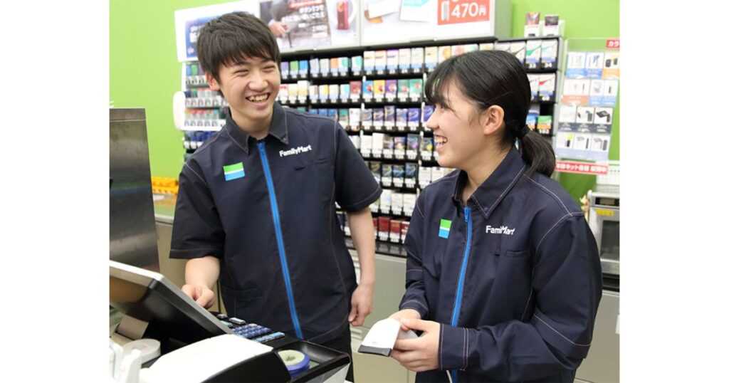 ファミリーマートのレジカウンター内で、笑顔で楽しく会話をしている男女のアルバイト店員