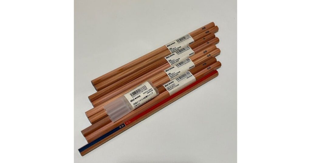 白い背景に斜めに並べられた、無印良品の木目調の裸鉛筆。それぞれの鉛筆に、硬度(HB, B, 2B, 4B)が書かれた小さな商品タグが付いている。中央左には、透明な「両端がつかえる鉛筆キャップ 2本入」の商品タグ付きパッケージが置かれている。