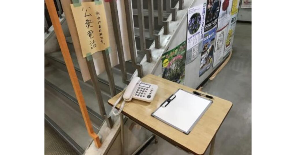 階段脇のテーブルに設置された、発信専用の災害用特設公衆電話と「かけるのみです」と書かれた案内紙