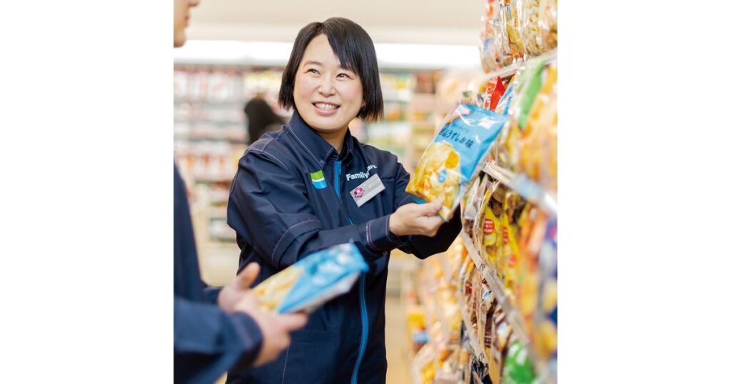 ファミリーマートの制服を着て、笑顔で品出しをする女性店員の写真