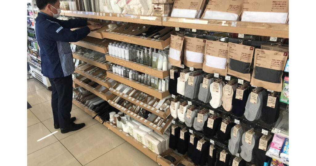 ローソンの店内で、無印良品の靴下やスキンケア用品が並ぶ陳列棚を整理している店員