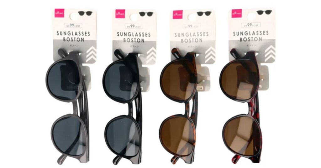 ダイソー(DAISO)で販売されているボストン型サングラス4種類。パッケージに「UV 99% CUT」と記載されており、グレー、黒、明るいべっ甲柄、暗いべっ甲柄のカラーバリエーションがフックに掛けられている状態。