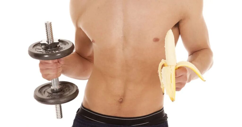 右手にダンベル、左手に剥いたバナナを持つ上半身裸の筋肉質な男性