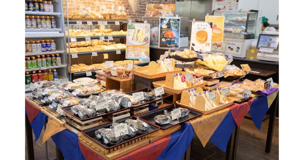 店内で調理された惣菜パンや塩バターパン、サンドイッチなどが手作り感のある平台や棚に並べられた、コンビニの店内ベーカリーコーナー