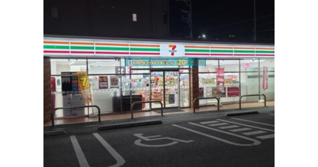 夜のコンビニエンスストアの外観。駐車場と、明かりがついた店舗が見える。