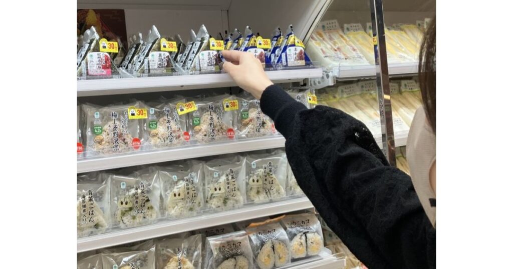 コンビニのおにぎりコーナーで商品を選んでいる女性の手元。