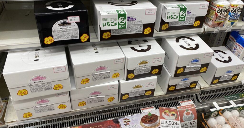 コンビニのスイーツ棚に並べられた、黄色い「半額」シールがいくつも貼られているクリスマスケーキの白い山積みボックス。