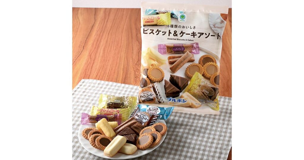 ファミリーマートの「ファミマル 6種類のおいしさ ビスケット&ケーキアソート」の大袋と、中身の個包装お菓子(ルマンドやバームロールなど)が皿に並んでいる様子。