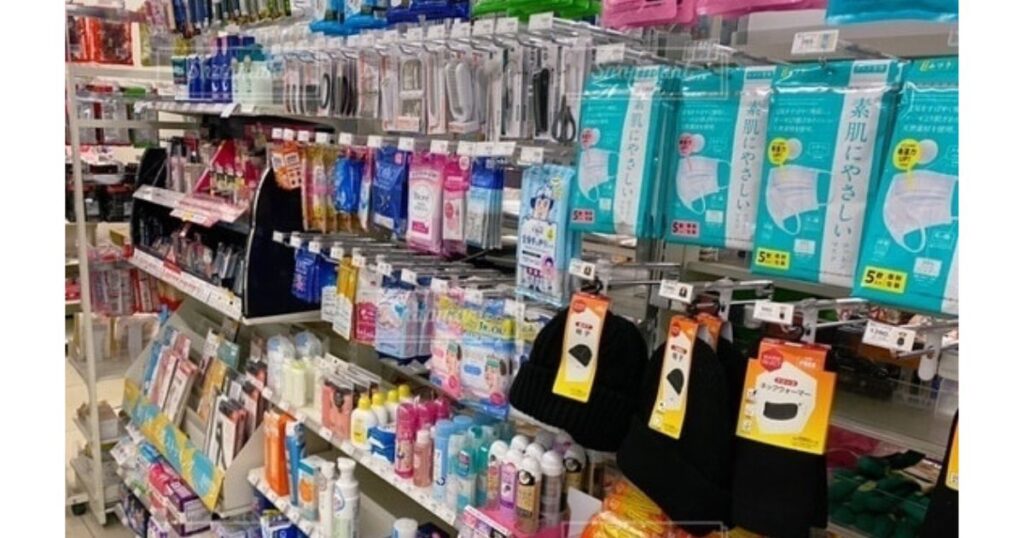 コンビニ店内の日用品・雑貨コーナー。マスクや帽子、日用小物が並ぶ、保冷バッグが販売されていることが多い売り場の様子。