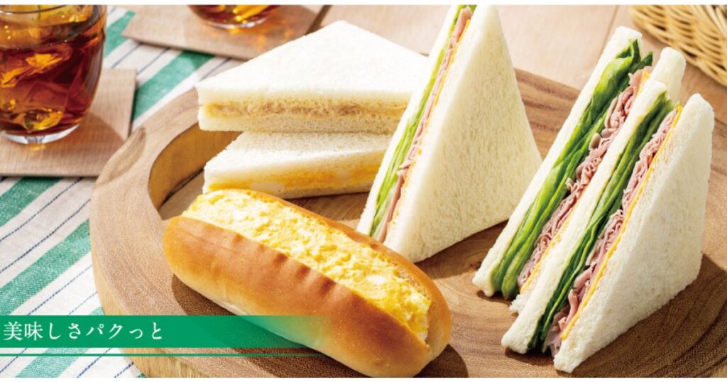 木製プレートに綺麗に盛り付けられた、コンビニの各種サンドイッチとたまごロールパンのイメージカット。