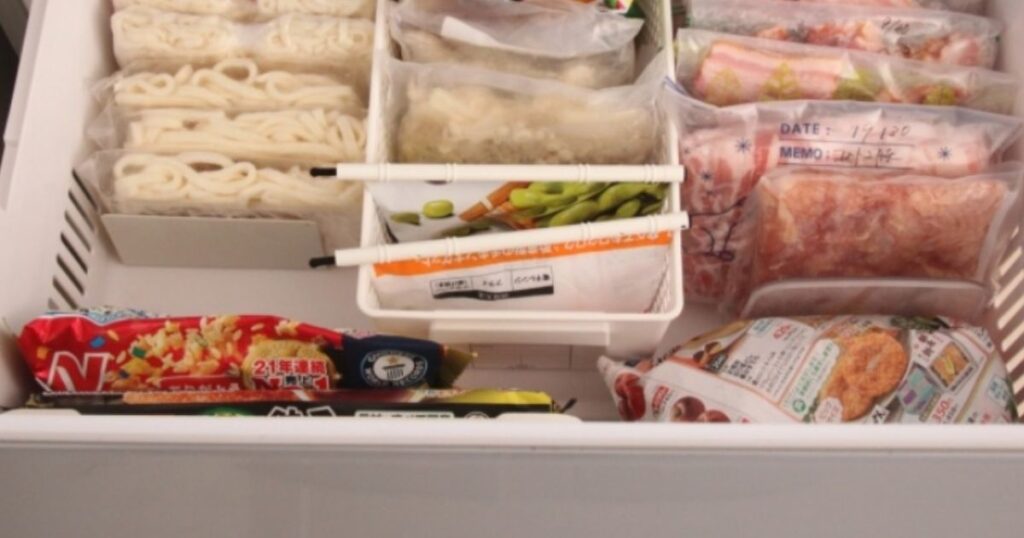 家庭用冷凍庫の引き出しの中で、仕切りを使って整然と立てて収納された冷凍食品や小分け保存された食材