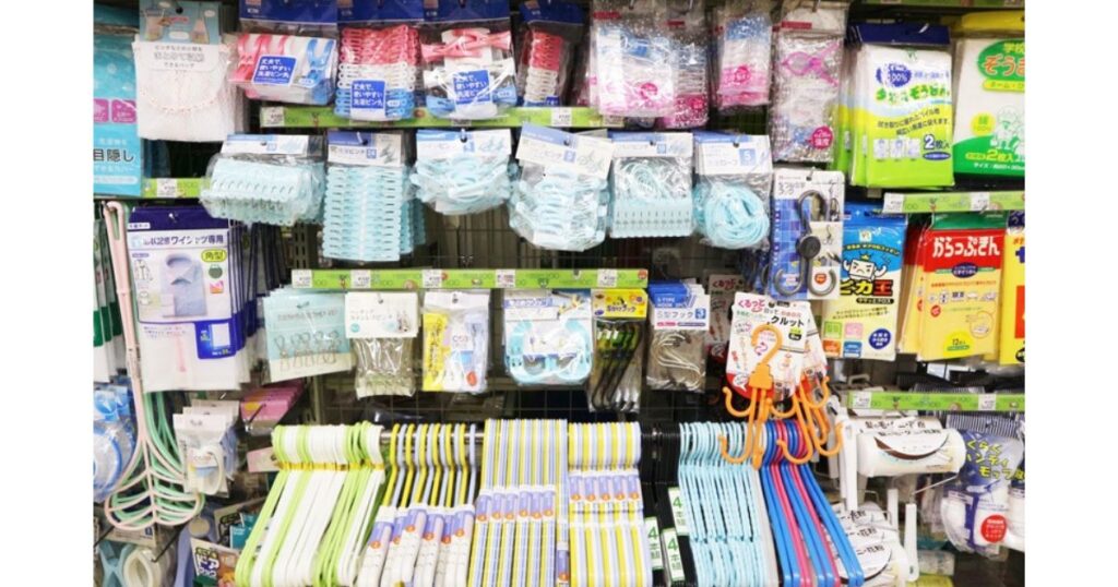 コンビニエンスストアの日用品売り場の様子。洗濯バサミ、ハンガー、掃除用品などの生活雑貨が所狭しと陳列されている棚の写真