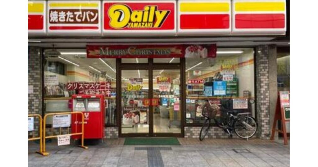 デイリーヤマザキの店舗入り口のすぐ左側に設置されている、赤い公設郵便ポストと店舗外観の写真。