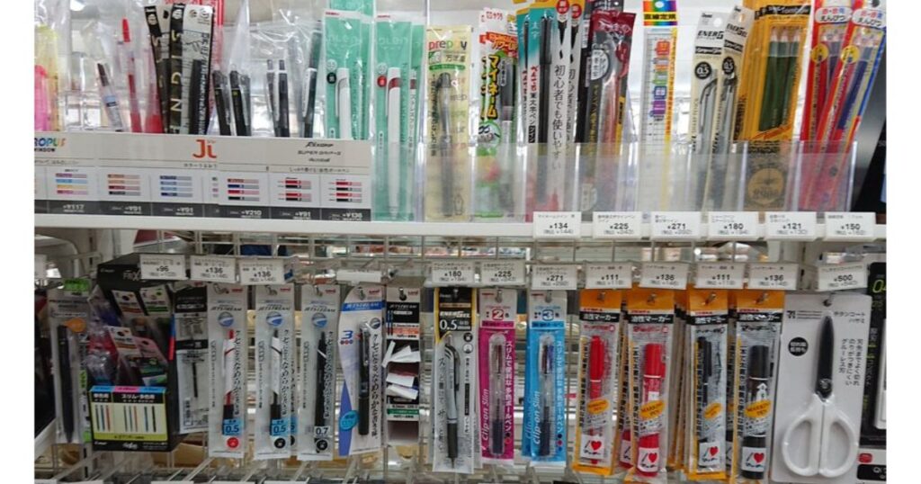 コンビニの文具コーナーの棚に並ぶ、各種ボールペンや多機能ペン、筆ペンの売り場写真。