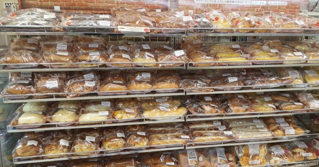 コンビニのパン売り場に、たくさんの種類のパンやサンドイッチが豊富に陳列されている様子