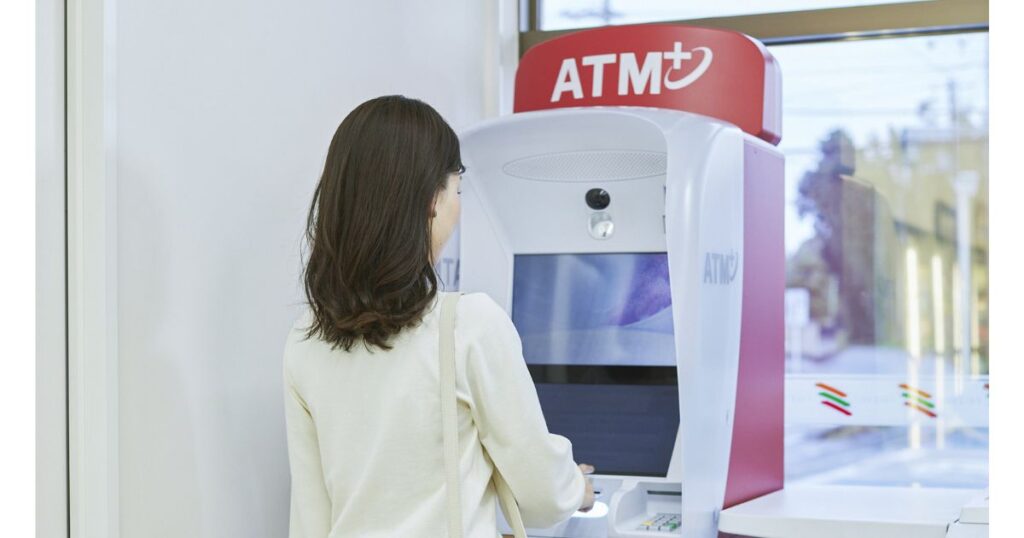 コンビニの店内に設置されたATM（現金自動預け払い機）の画面を操作している女性の後ろ姿