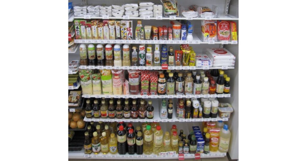 コンビニエンスストアの店内に陳列された、多数の調味料やドレッシング、ソースなどが並ぶ棚の写真。