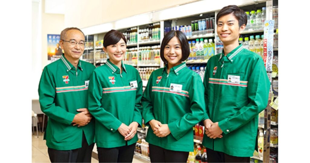 セブン-イレブンの制服を着て笑顔で並ぶ、自然な黒髪や暗い茶髪の従業員4人