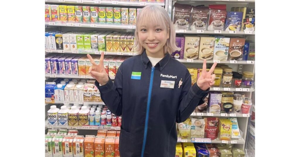 ファミリーマートの制服を着て笑顔でピースサインをする、明るい髪色の女性従業員