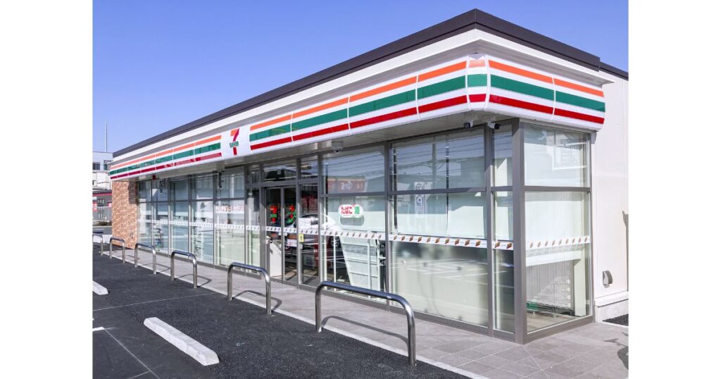 セブン-イレブンの店舗外観。青空の下に建つ標準的なコンビニの建物と駐車場の風景