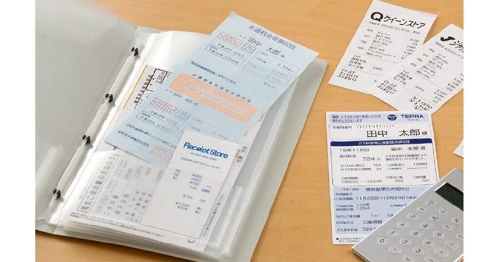 机の上に広げられた様々な領収書や公共料金の払込受領証。横には電卓と、それらを整理・保管するための書類用クリアファイルが置かれている、経理事務をイメージした写真。