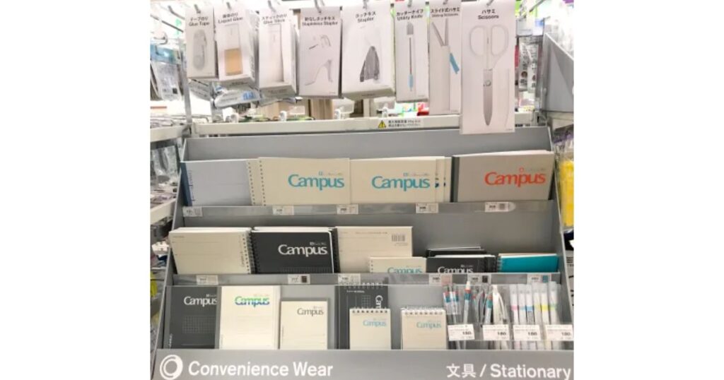 コンビニの文房具・日用品売り場の棚。ハサミやカッターナイフ、Campusノートなどが陳列されている様子。