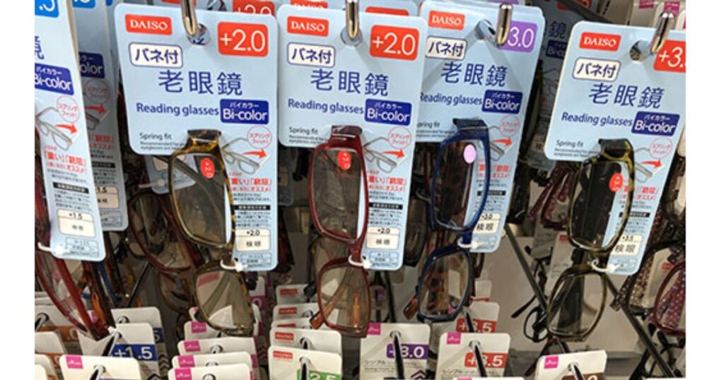 ダイソーの店頭フックに並ぶ、度数「+2.0」や「+3.0」のバネ付き既製老眼鏡