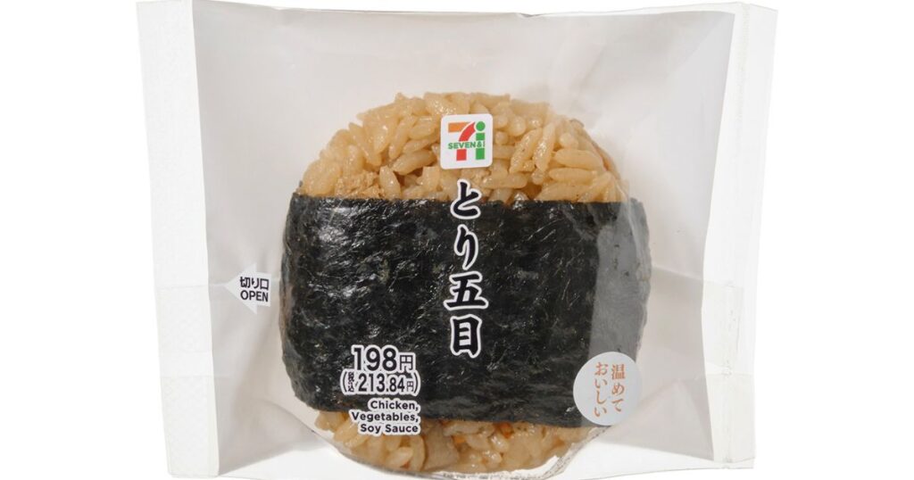 セブン-イレブンのパッケージに入った「とり五目」おにぎりの写真。海苔が巻かれており、価格や「温めておいしい」のラベル、英語の具材表記が見える。
