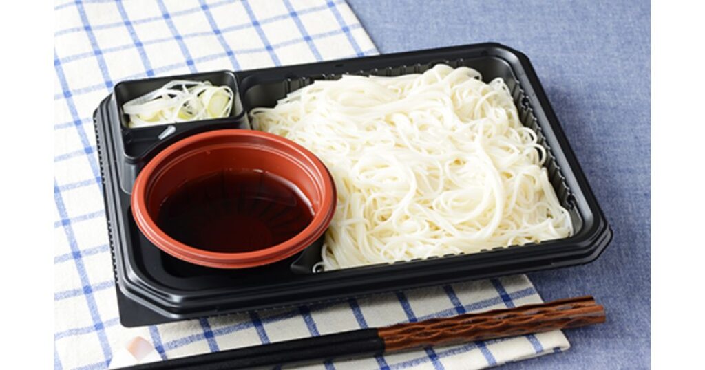 黒いプラスチック容器に盛り付けられた白いそうめんと、薬味のネギ、濃い茶色のめんつゆのチルド麺調理例