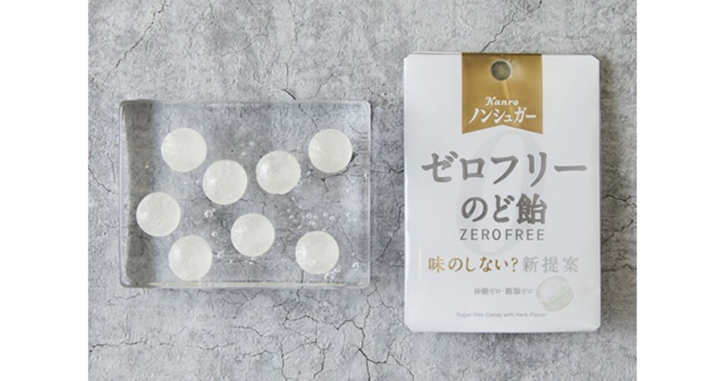 カンロ「ノンシュガー ゼロフリーのど飴」の白いパッケージと、ガラス皿に並べられた透明な飴の粒。「味のしない?新提案」の文字。