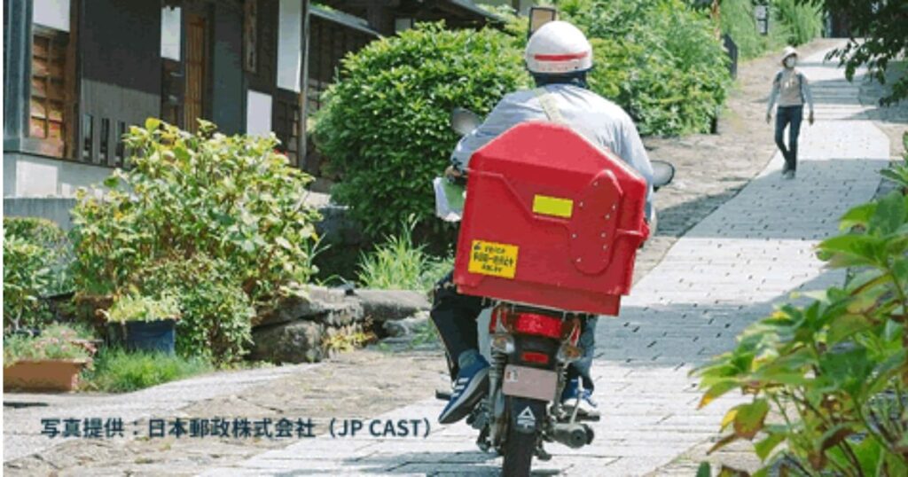 石畳の坂道を赤い配送ボックスを載せて走る日本郵便の配達バイクを、後ろから撮影した写真（写真提供：日本郵政株式会社）。