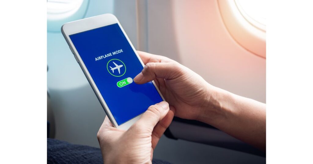 飛行機の窓際でスマートフォンの画面に表示された「AIRPLANE MODE（機内モード）」をオンにする手元