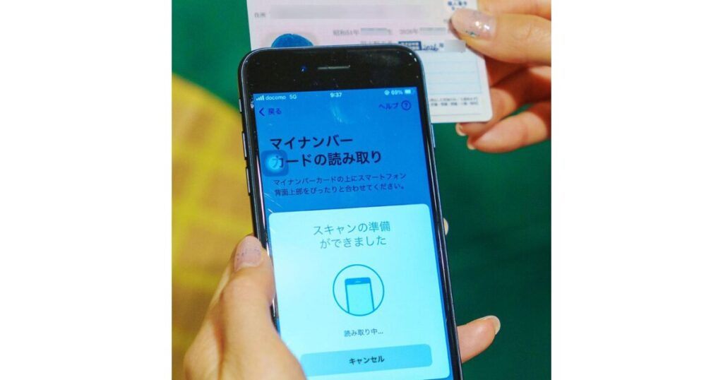 スマートフォンのアプリ画面にマイナンバーカードをかざして、年齢確認用のICチップデータを読み取っている様子。